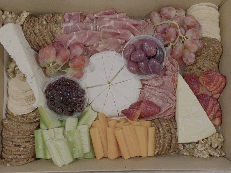 A catering box of cured meats, cheeses, grapes and crackers